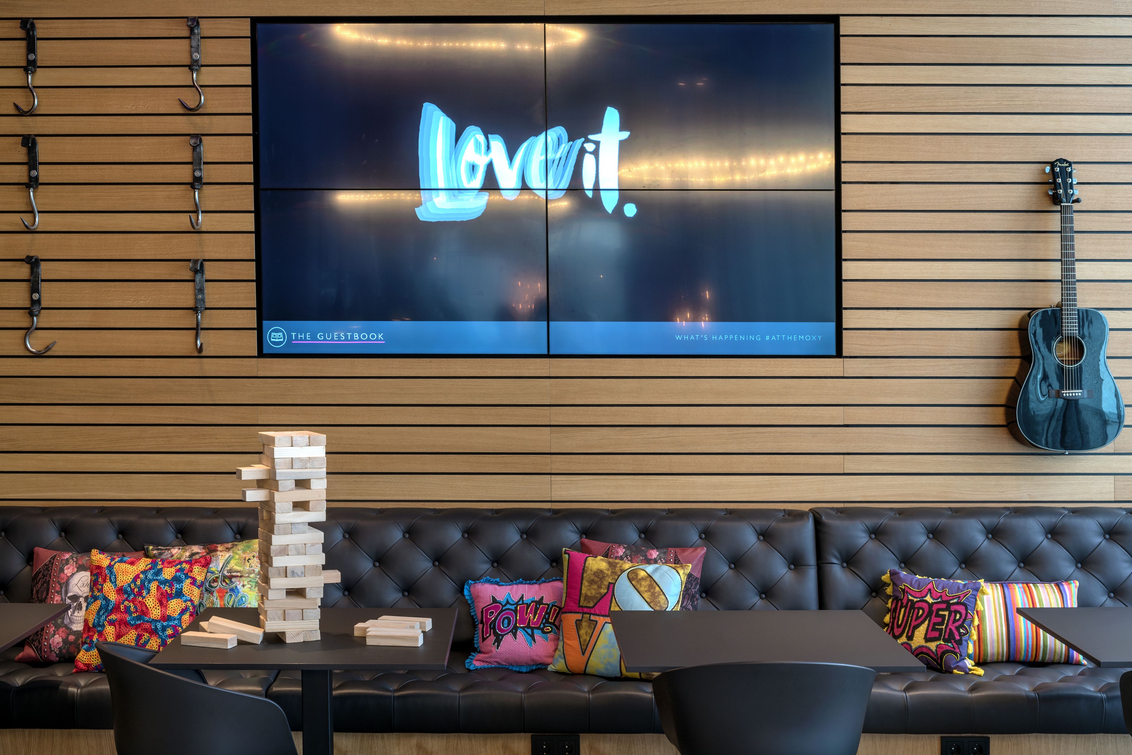 Una habitación moderna con una televisión mostrando 'Love It', una torre de Jenga y una guitarra.
