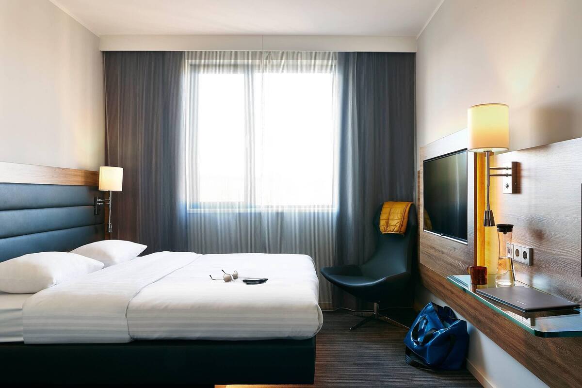 Ein Hotelzimmer mit einem Bett, einem Schreibtisch mit Lampe, einem Sessel und einem Fernseher.