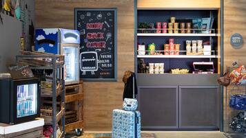 A cozy corner with a chalkboard sign reading "MOXY SNACK CORNER," a vending machine, and a selection of snacks and drinks on shelves.