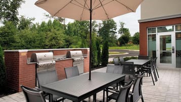 Une terrasse extérieure équipée d’un barbecue, de sièges et d’un parasol.