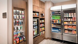 Eine Selbstbedienungsstation für Getränke und Snacks mit gekühlten und ungekühlten Optionen, darunter Wasserflaschen, Säfte und verschiedene Snacks.