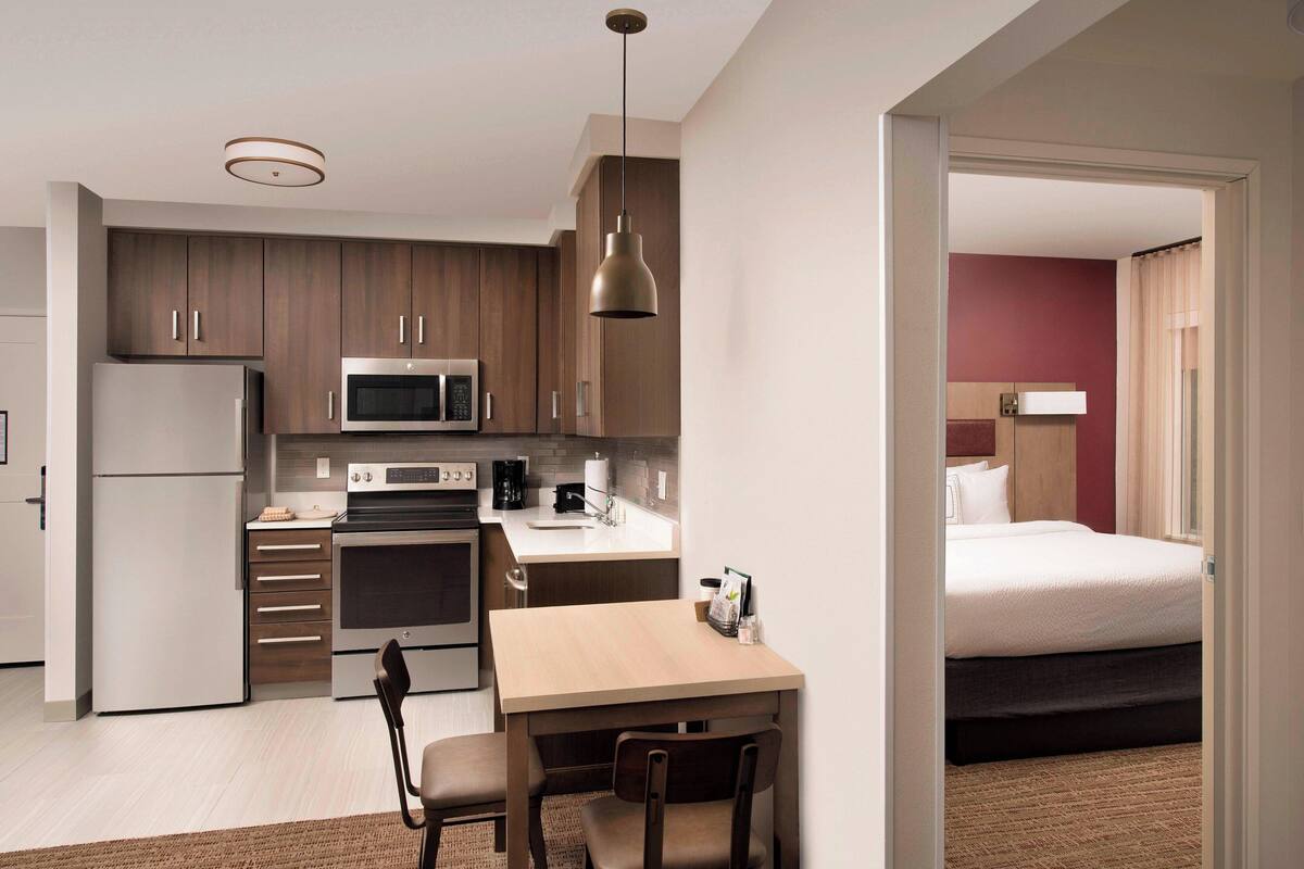 A compact hotel room with a kitchenette, a bed, and a view of the outside.