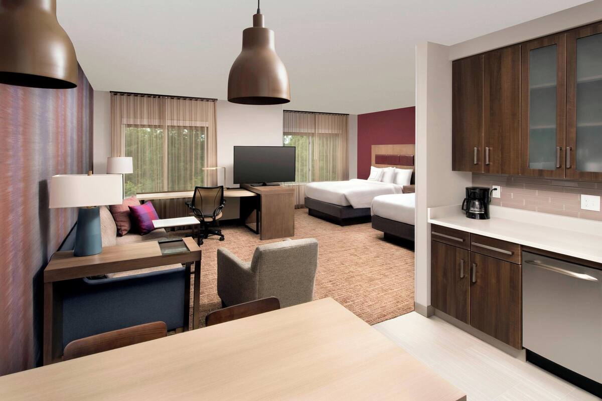 A hotel room with a bed, desk, chair, television, and kitchenette.