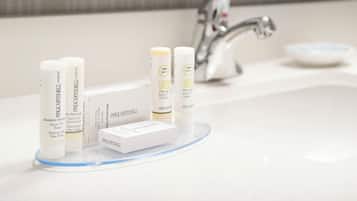 Un lavamanos de baño con artículos de aseo personal, incluyendo champú, acondicionador y gel de ducha.
