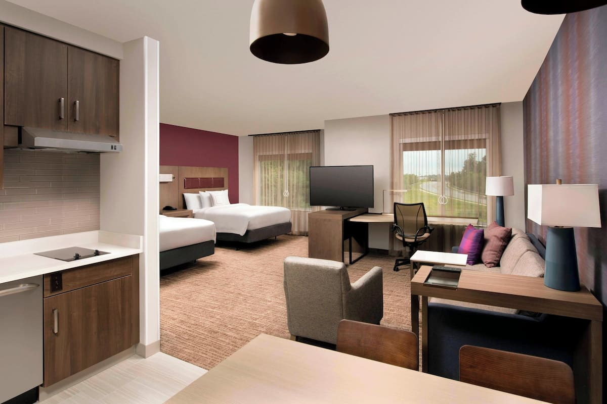 A hotel room with a kitchenette, a bed, a desk, a TV, and a sofa.