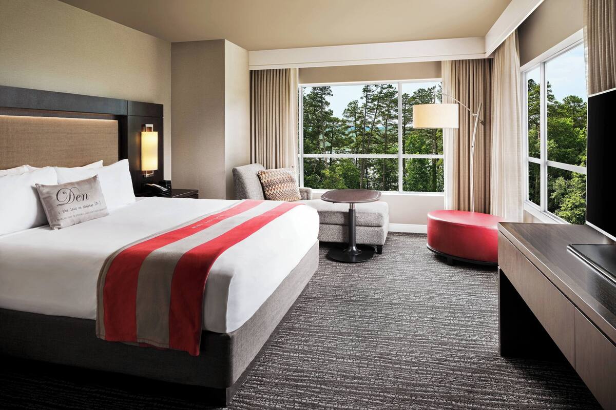 A hotel room with a large bed, a desk, a chair, a small table, and a TV.