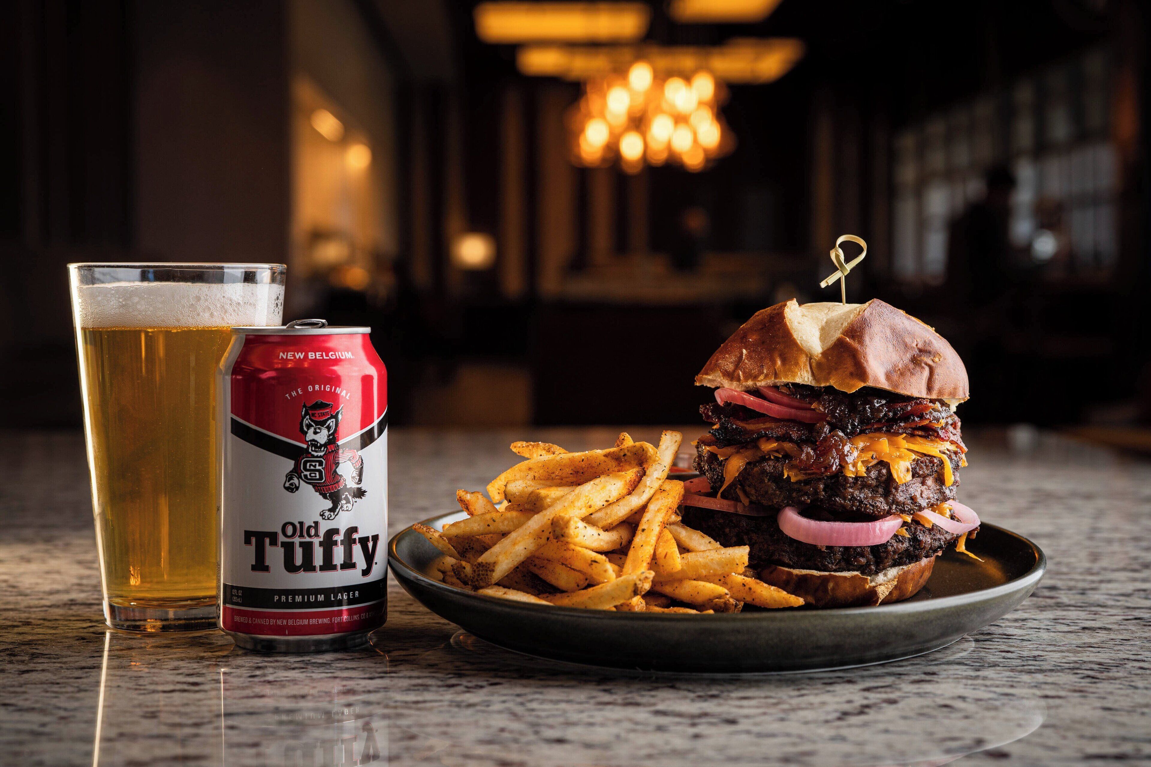 Un repas composé d'un hamburger, de frites et d'un verre de bière, accompagné d'une canette de bière Old Tuffy.