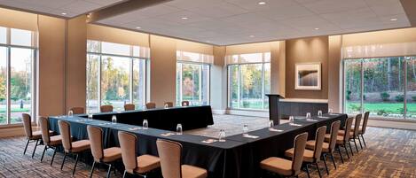A conference room with a long table, chairs, and large windows with a view of trees.