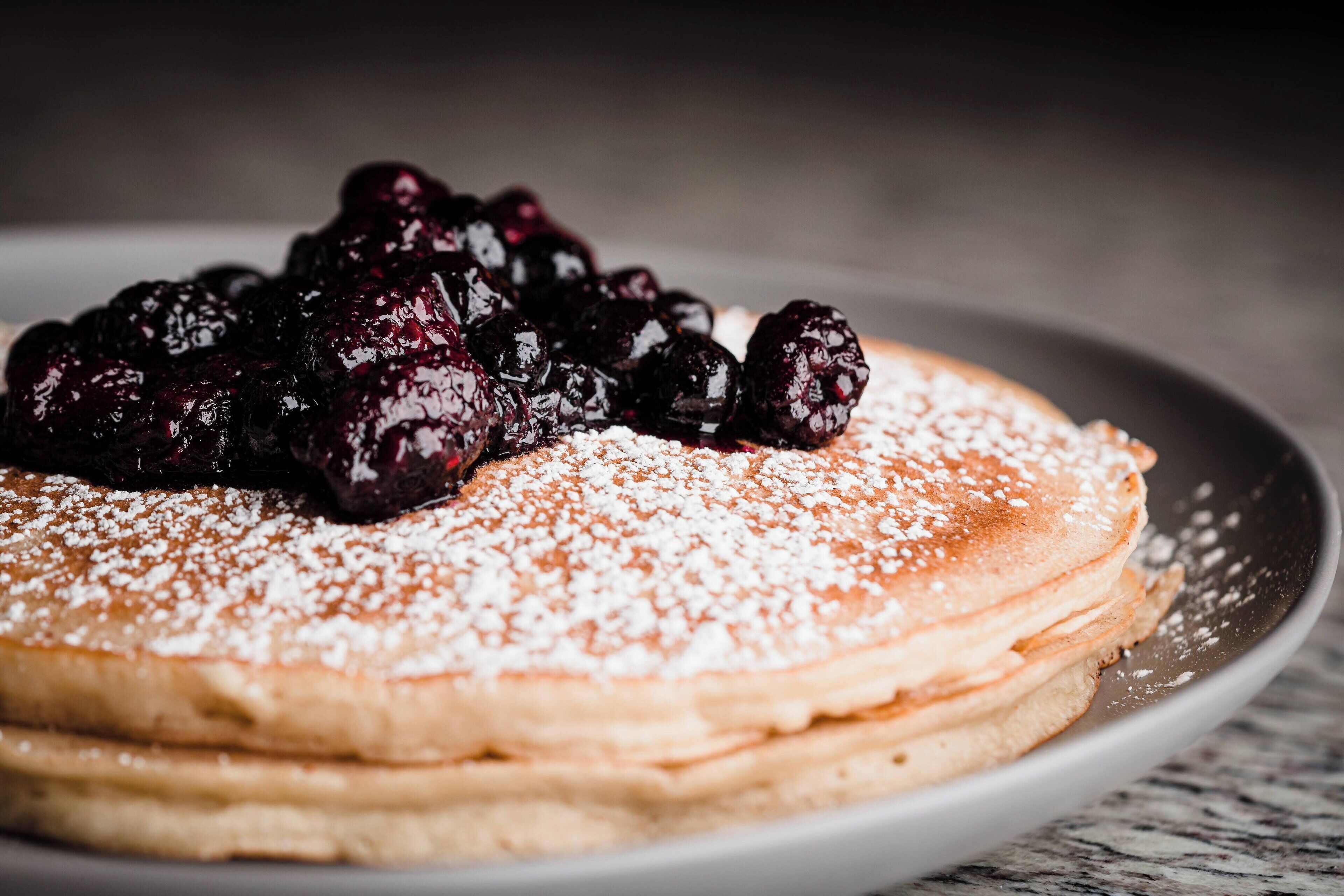 A stack of pancakes topped with blueberries and powdered sugar.
