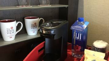 A coffee station with a coffee maker, two mugs, a water bottle, and a coffee pod.