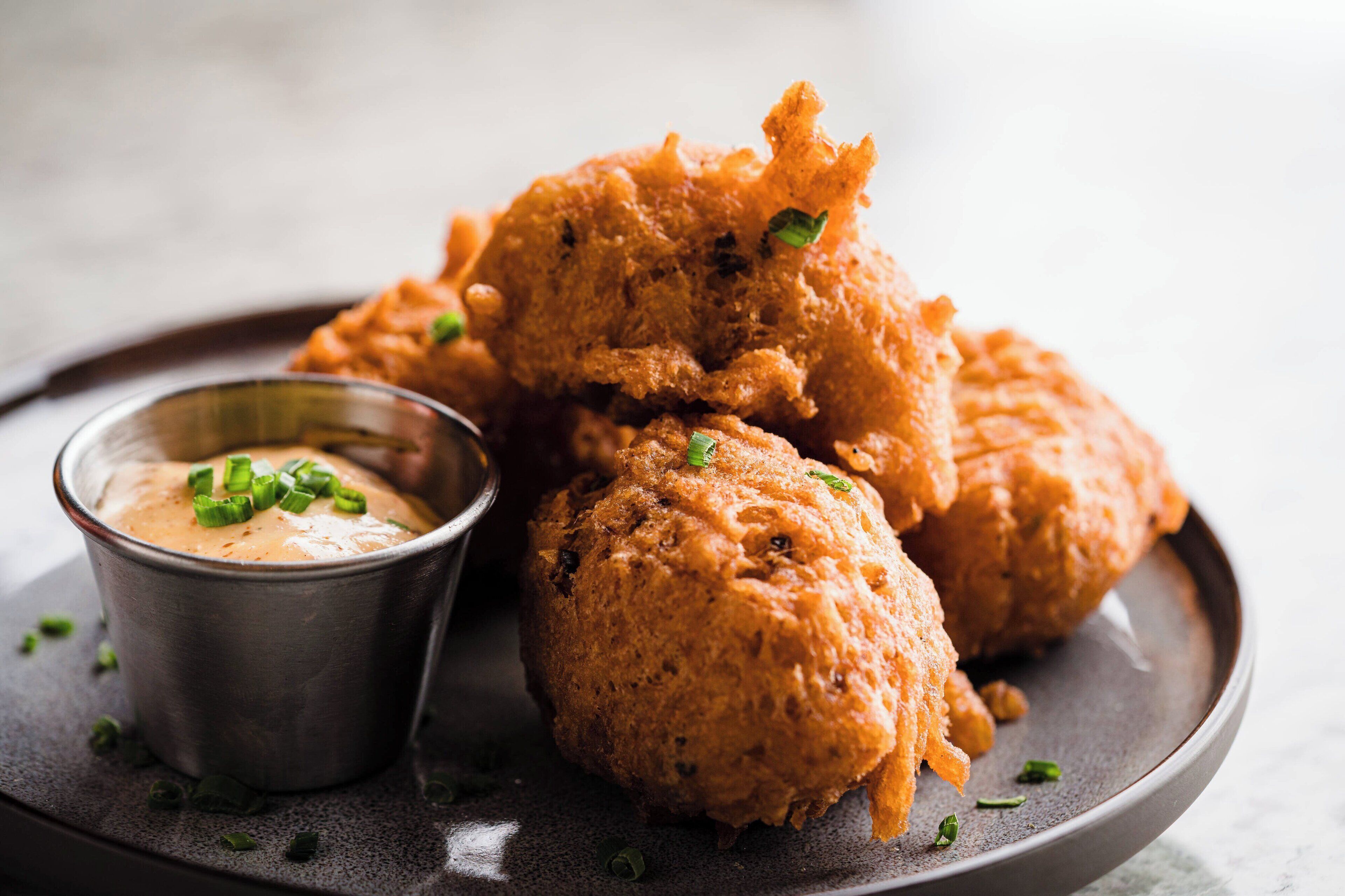 A plate of fried food with a dipping sauce and a small metal cup.