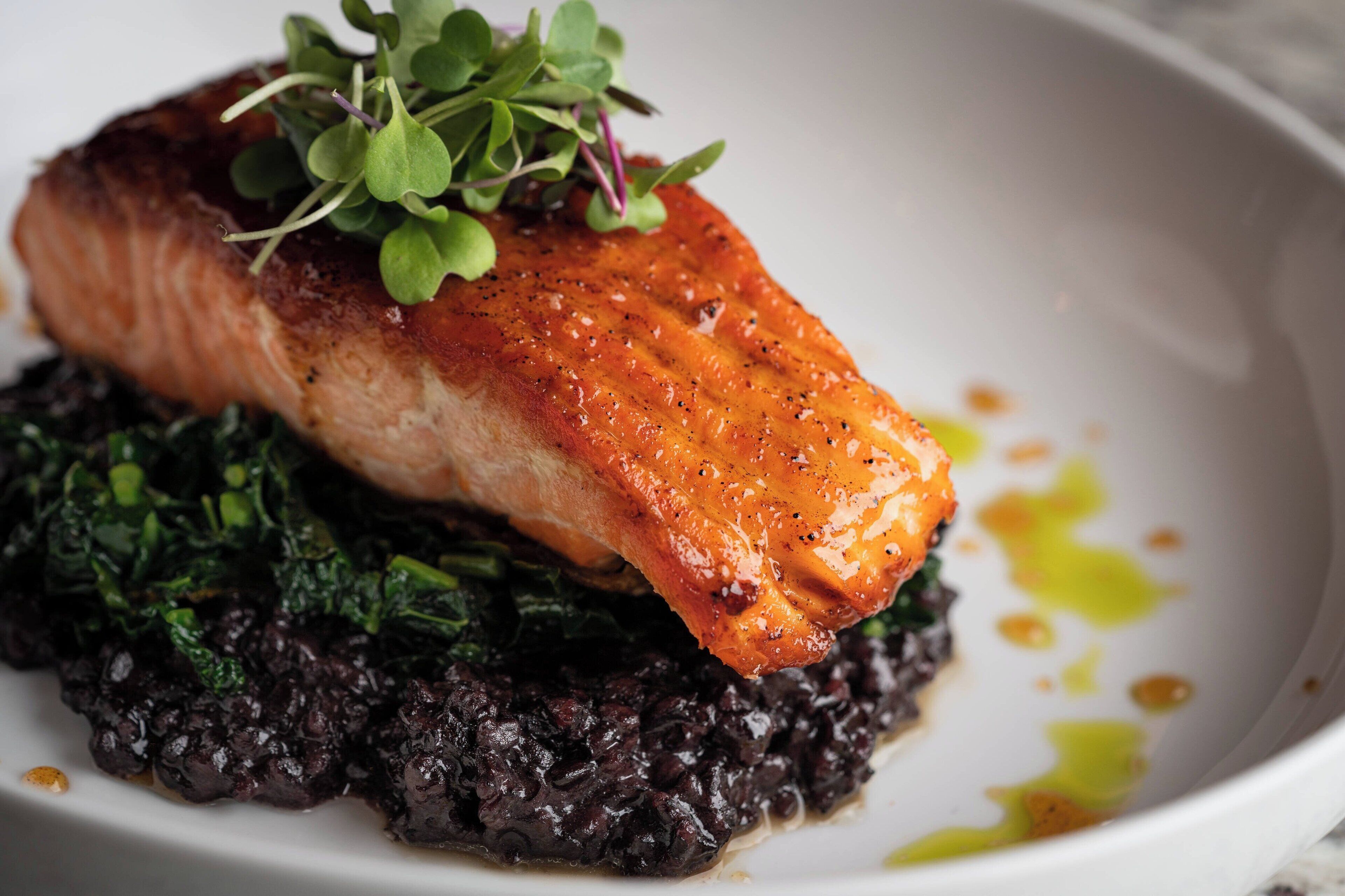 Un plato de salmón, risotto negro y vegetales verdes.