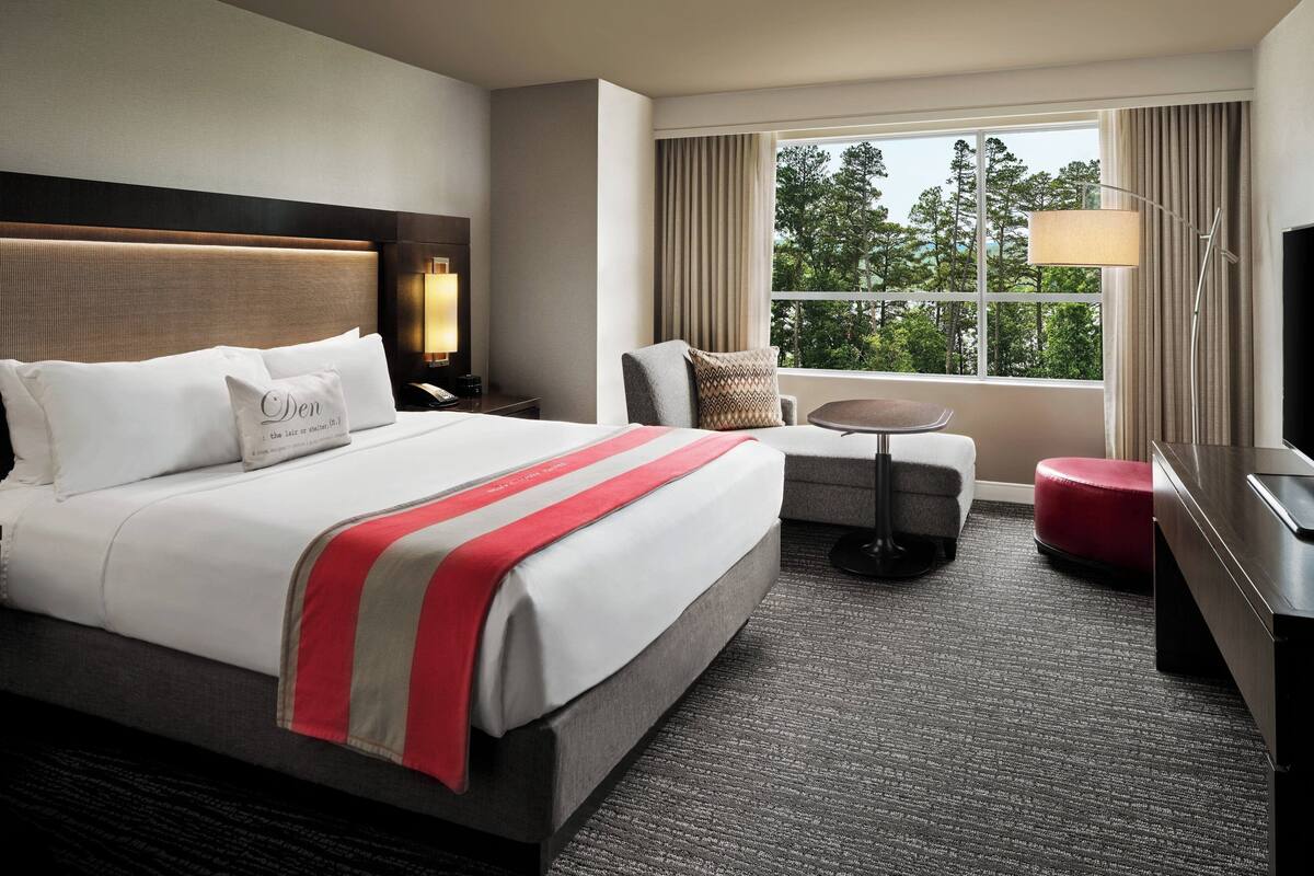 A hotel room with a large bed, a desk, a chair, a small table, and a TV.