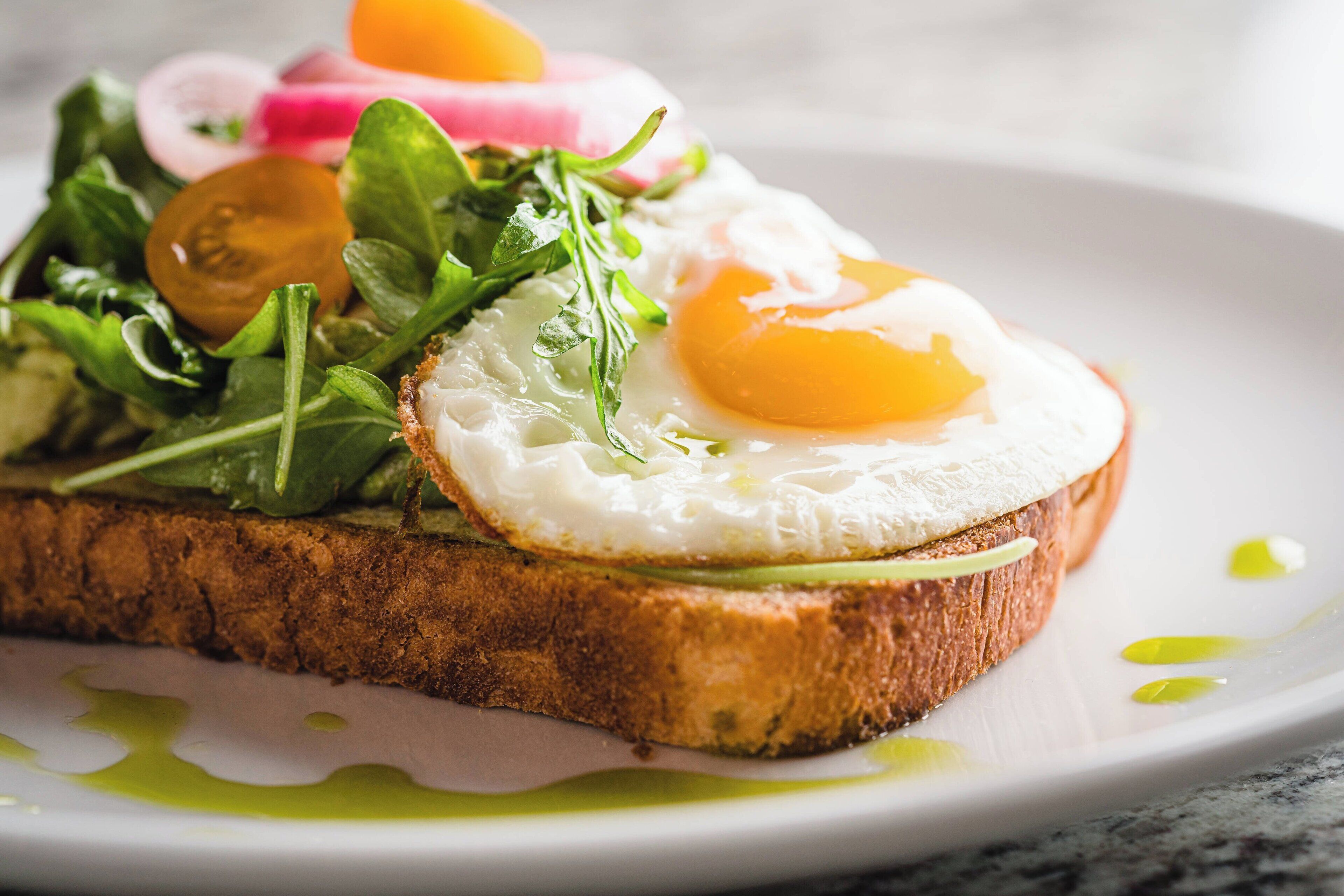 A breakfast dish with toast, egg, greens, and radish slices.