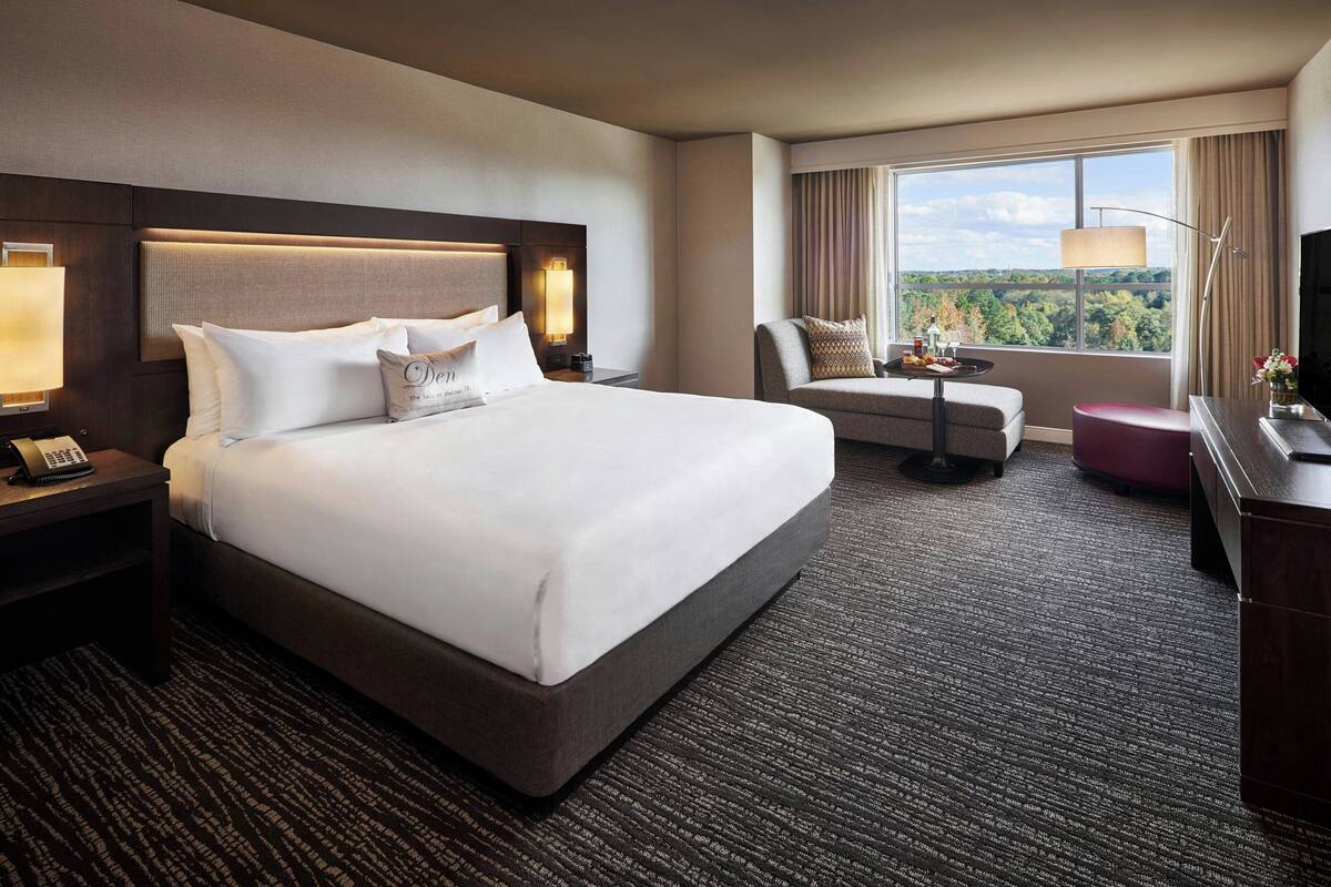 A hotel room with a large bed, a desk, a chair, and a view of the outdoors.