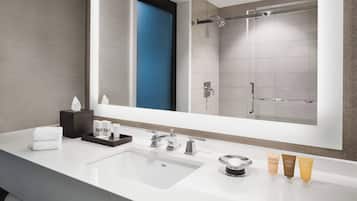 A modern bathroom with a large mirror, a white sink, and a shower area.