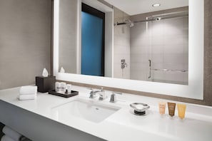 A modern bathroom with a large mirror, a white sink, and a shower area.