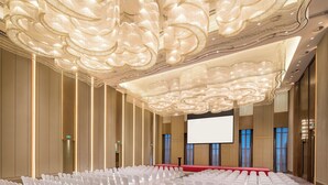 A conference room with rows of white chairs, a large screen, and ornate chandeliers. - Crowne Plaza Harbin Songbei by IHG (Harbin)