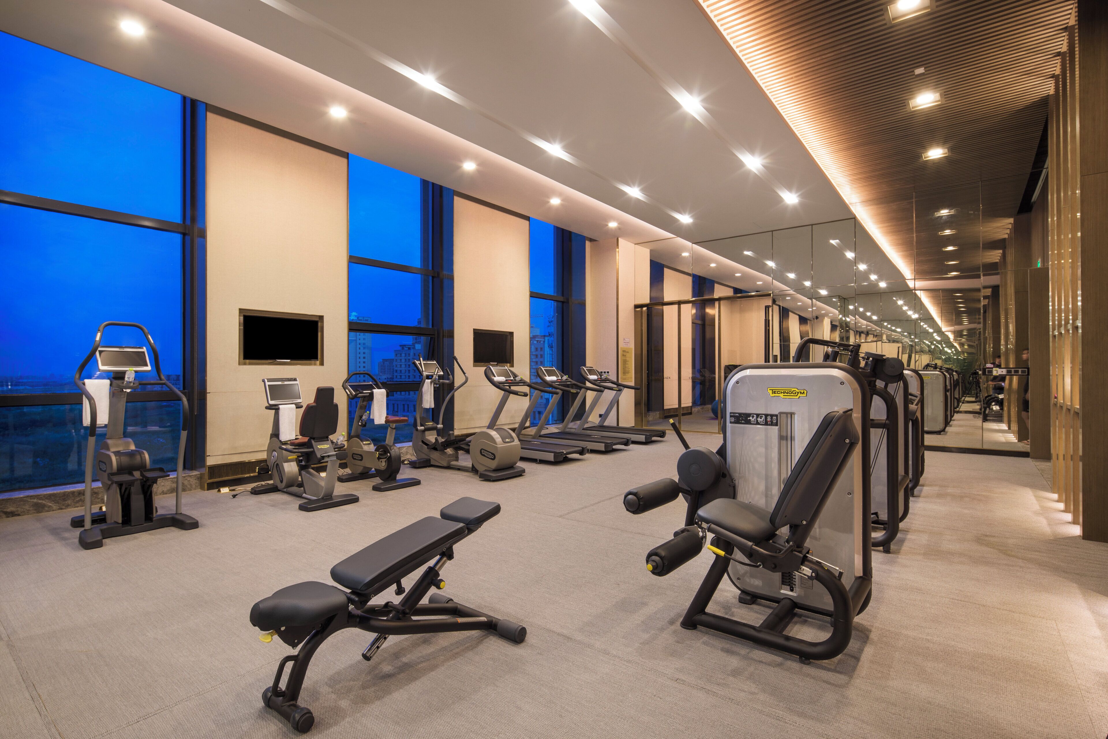 Ein modernes Fitnessstudio mit unterschiedlichen Trainingsgeräten, großen Fenstern und einer hohen Decke.