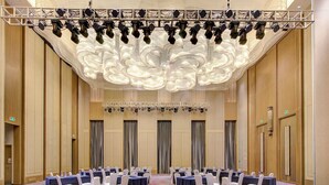 A conference room with rows of tables and chairs, a stage with lighting, and a large decorative ceiling. - Crowne Plaza Harbin Songbei by IHG (Harbin)