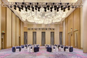 A conference room with rows of tables and chairs, a stage with lighting, and a large decorative ceiling. - Crowne Plaza Harbin Songbei by IHG (Harbin)