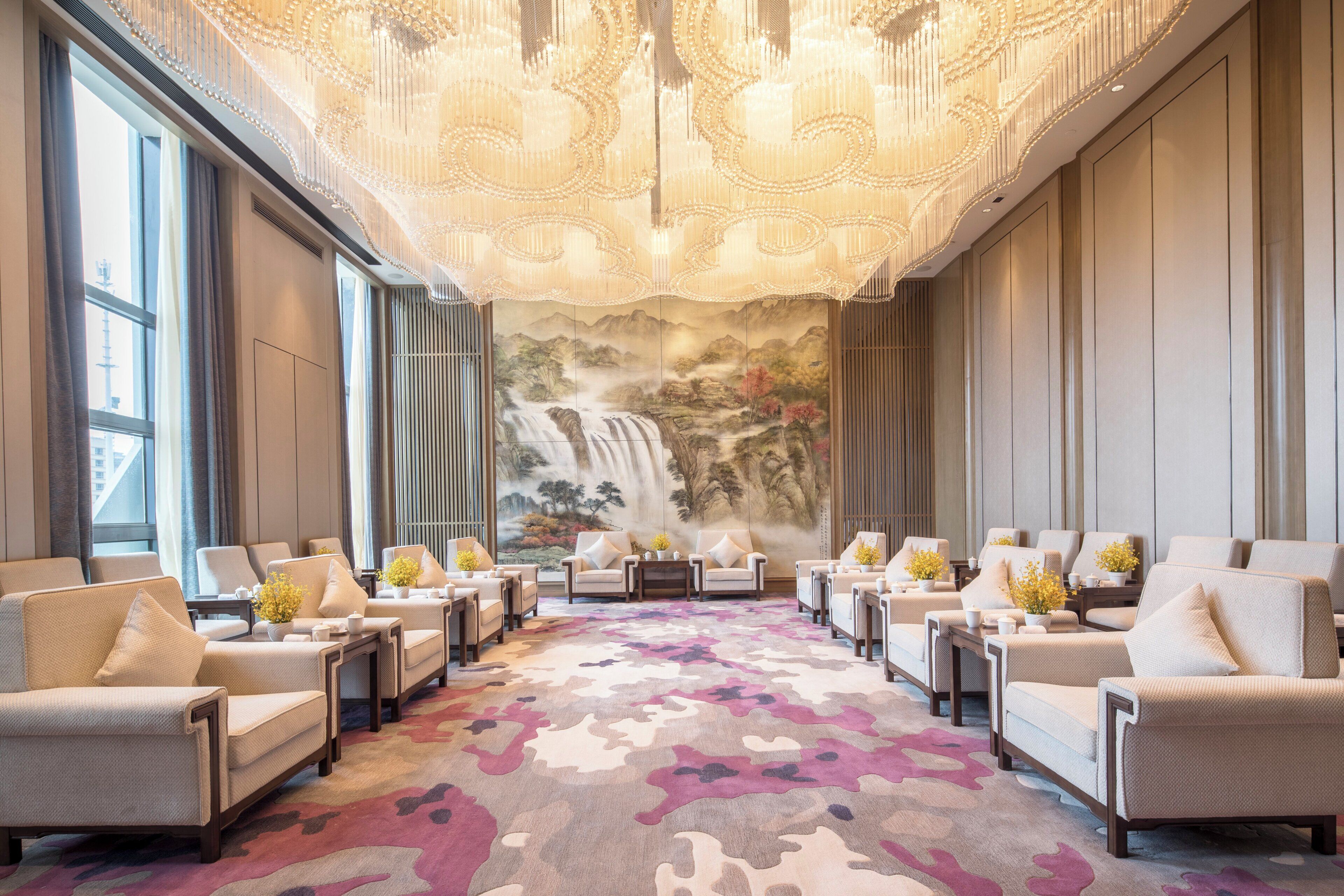 Un vestíbulo de hotel con un amplio espacio de estar, un mural de cascada y una alfombra estampada.