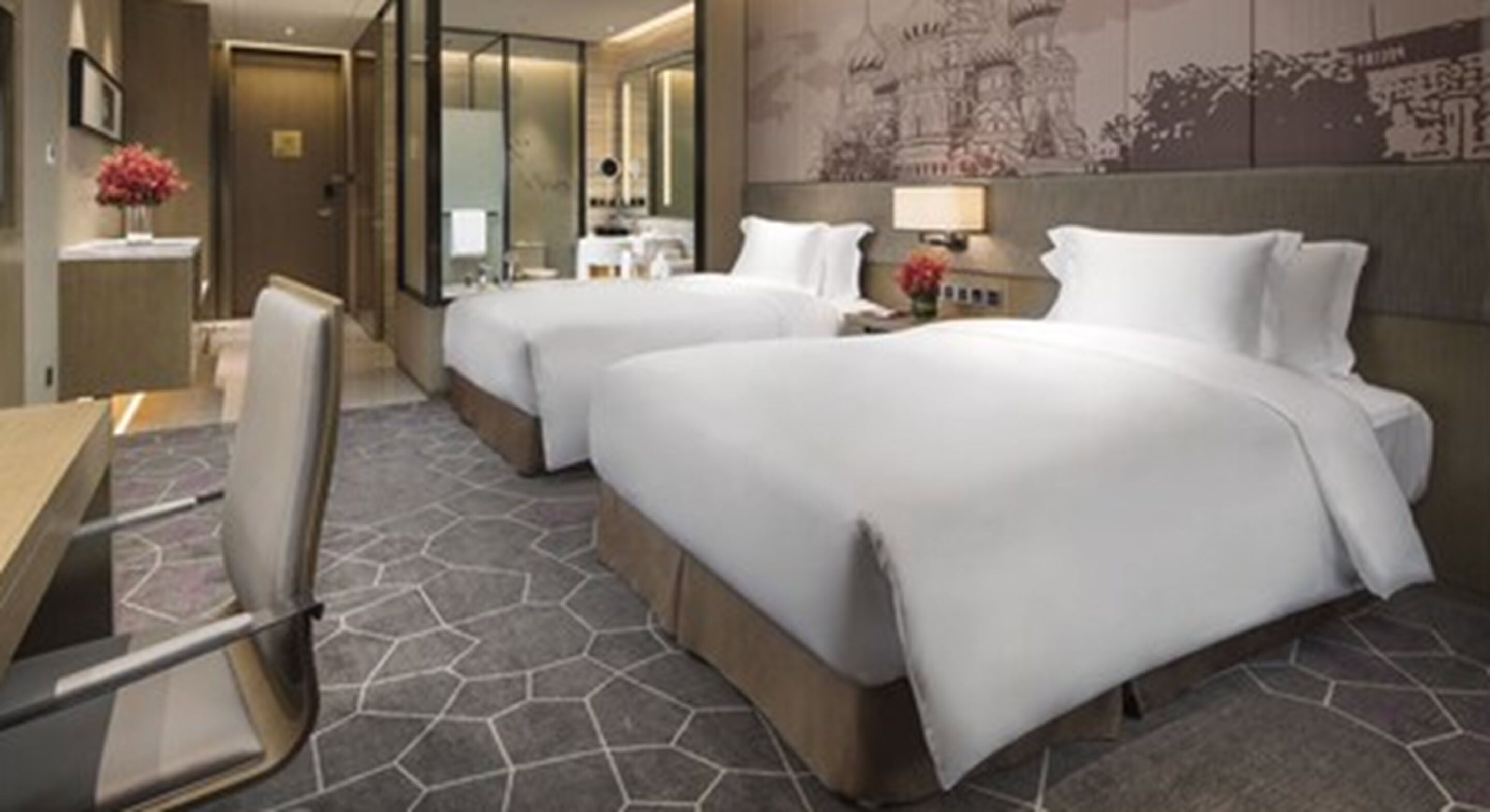 Une chambre d’hôtel avec deux lits, un bureau, une chaise et une salle de bain visible à travers une porte en verre.