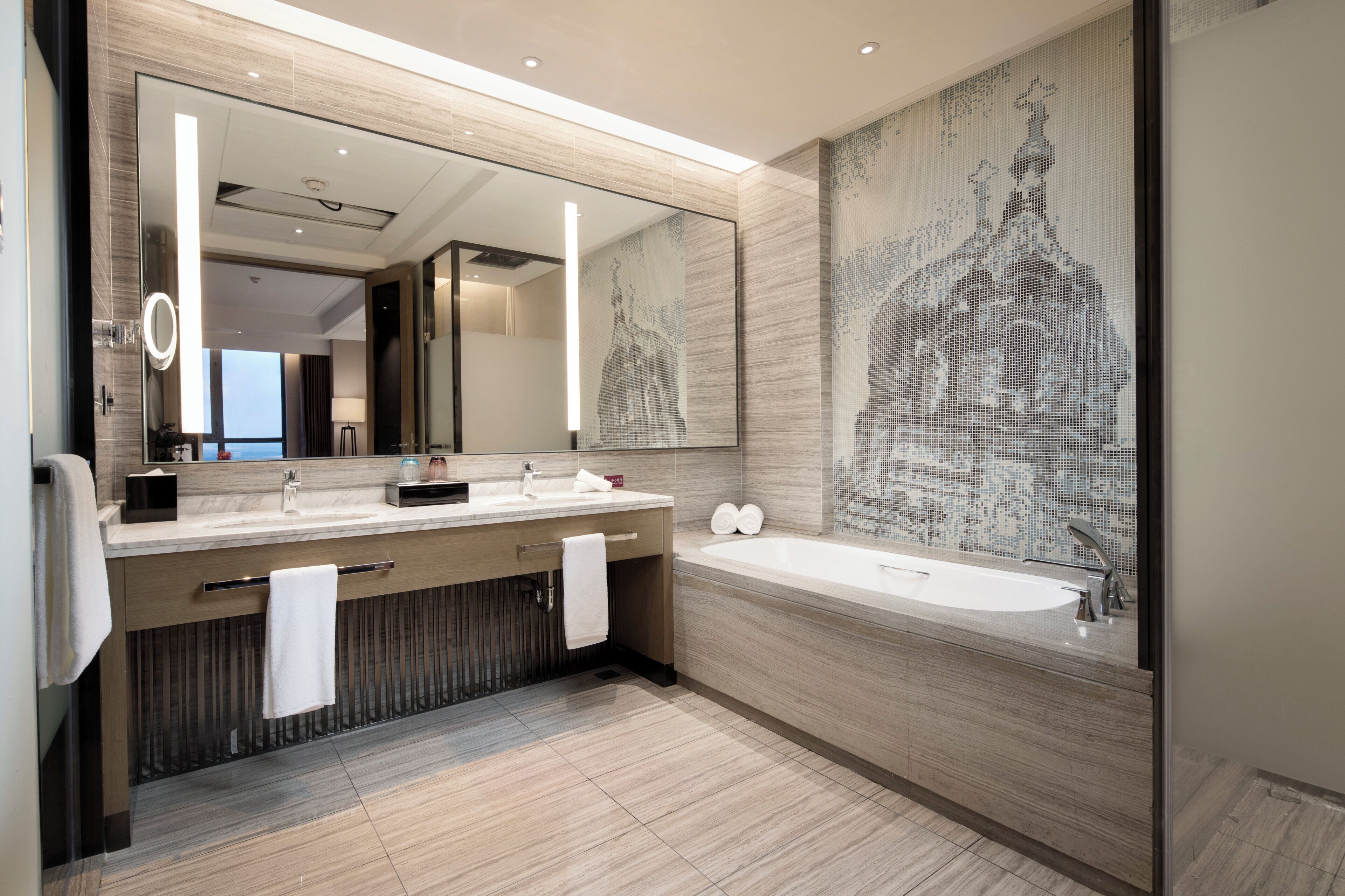 Un baño moderno con un espejo grande, un lavabo doble y una bañera independiente.