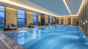 A modern indoor swimming pool with clear blue water, large windows, and comfortable seating along the sides. - Crowne Plaza Harbin Songbei by IHG (Harbin)