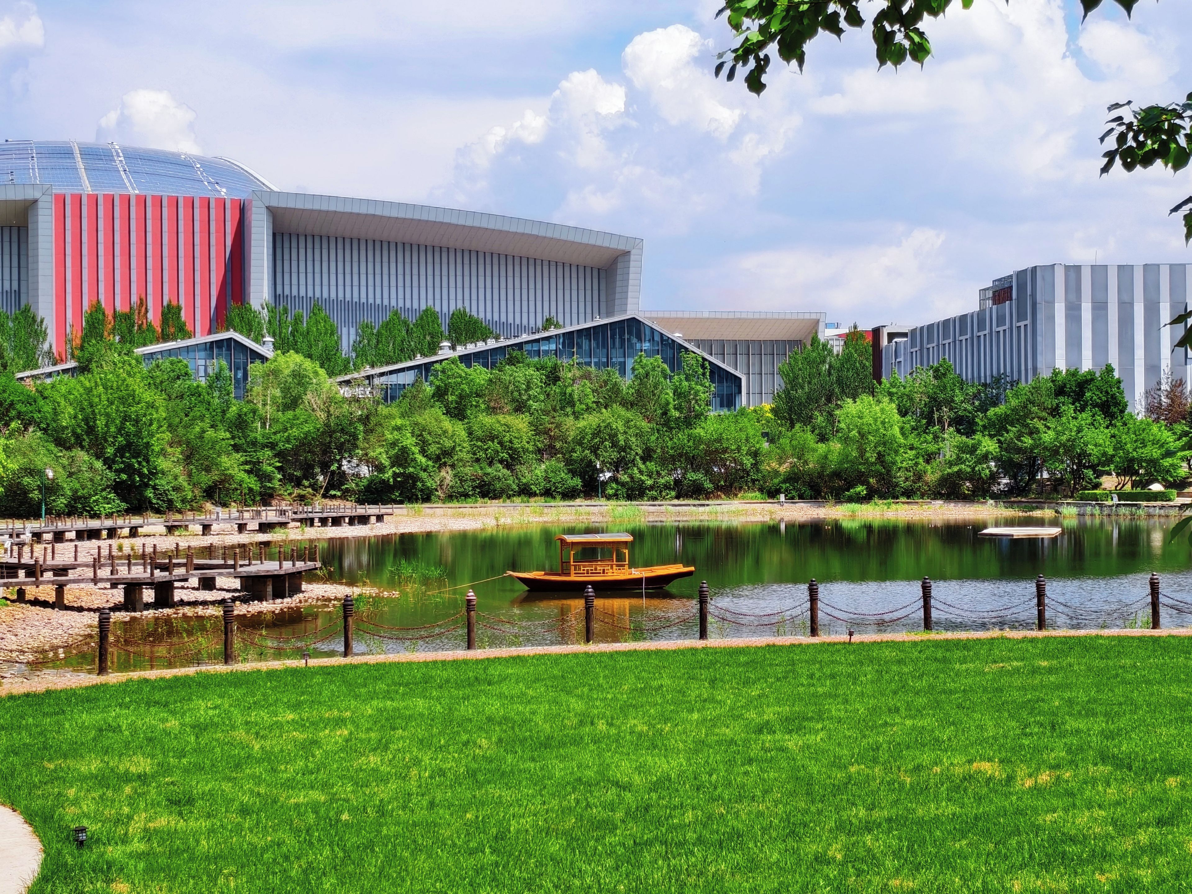 A modern building with a glass facade, a body of water with a boat, and a grassy area.
