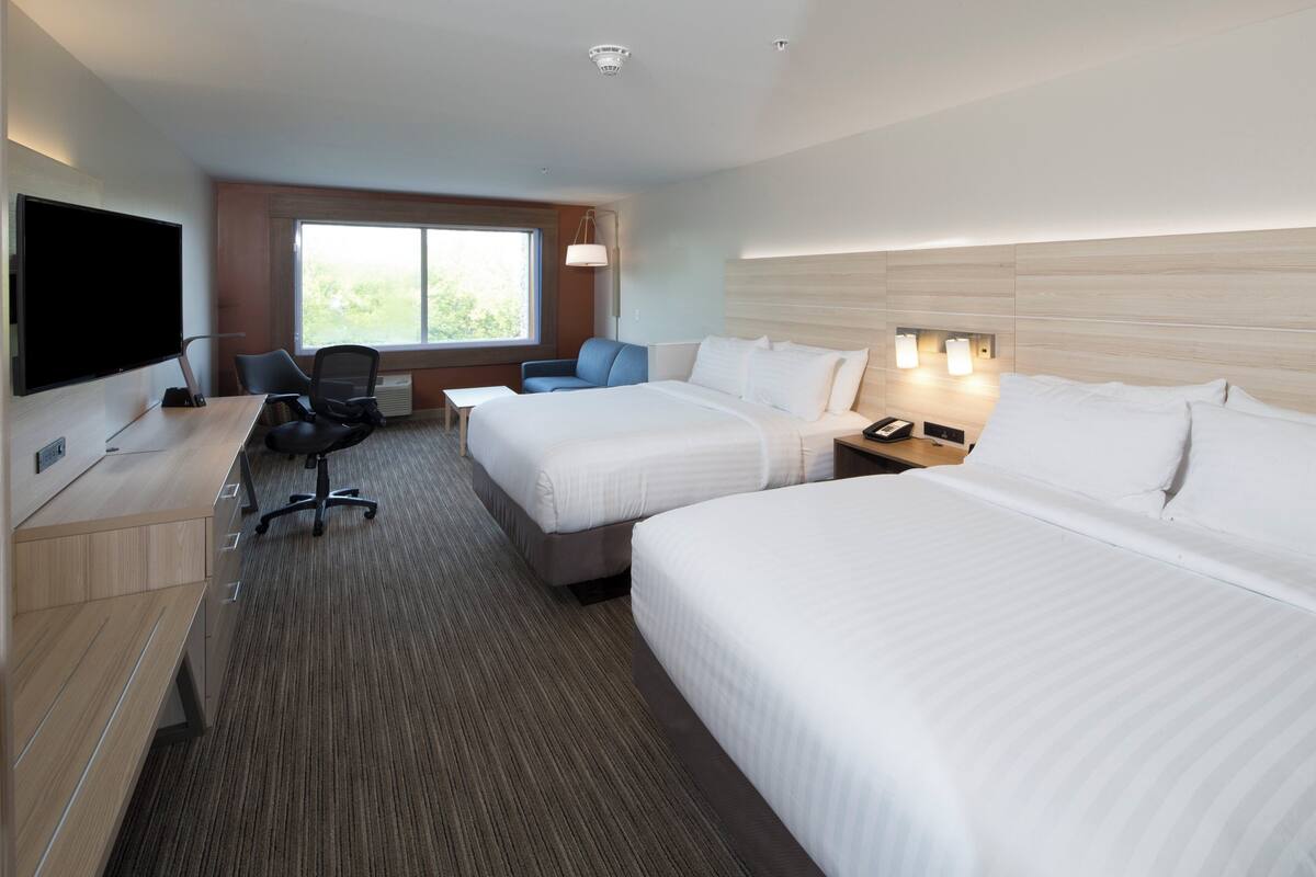 Habitación de hotel con dos camas, un escritorio con computadora, televisor y ventana grande.