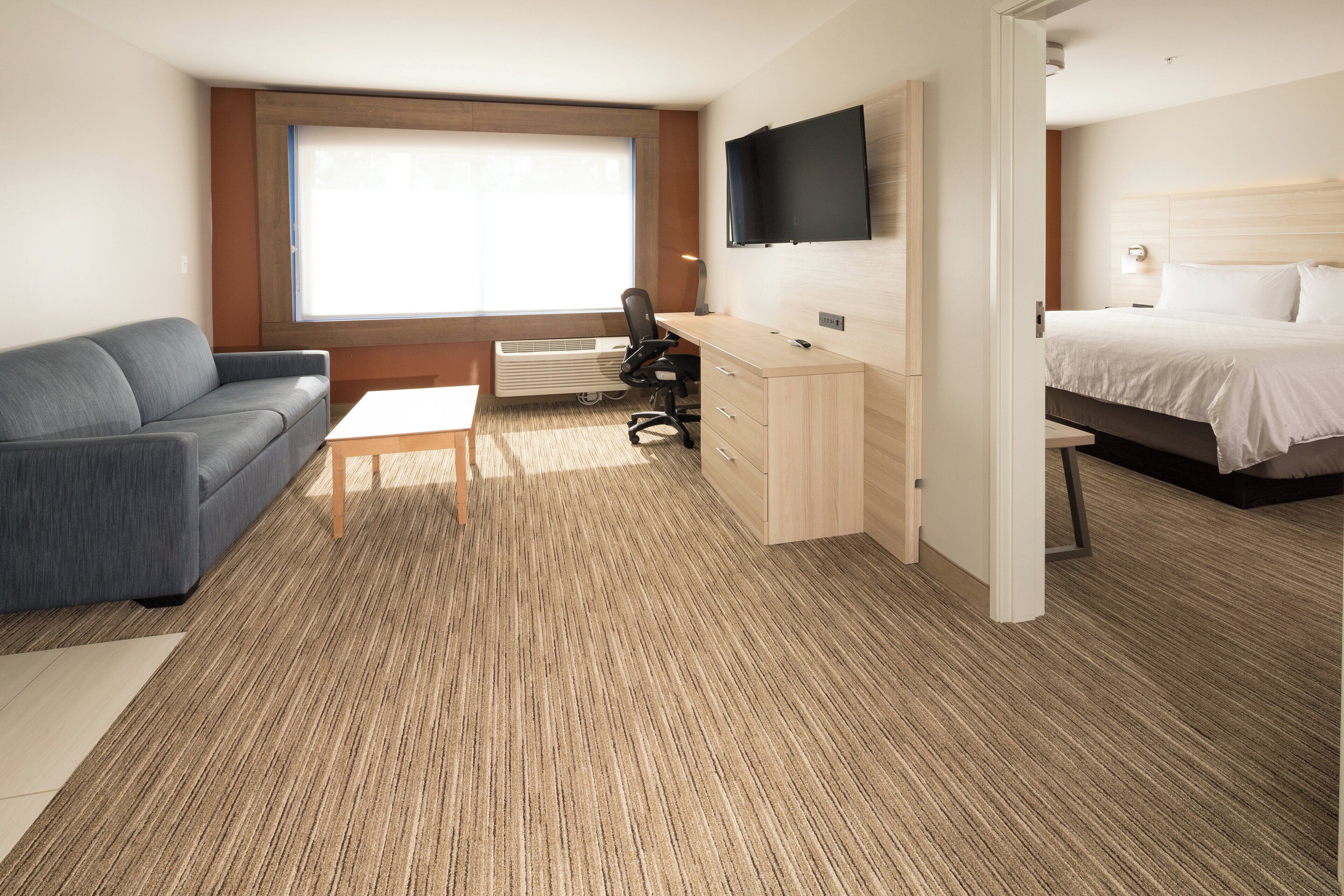 A hotel room with a bed, a desk, a chair, a sofa, and a TV.