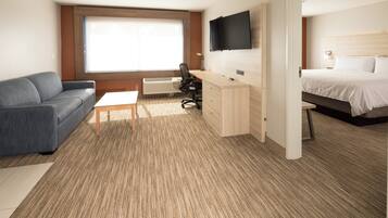 A hotel room with a bed, a desk, a chair, a sofa, and a TV.