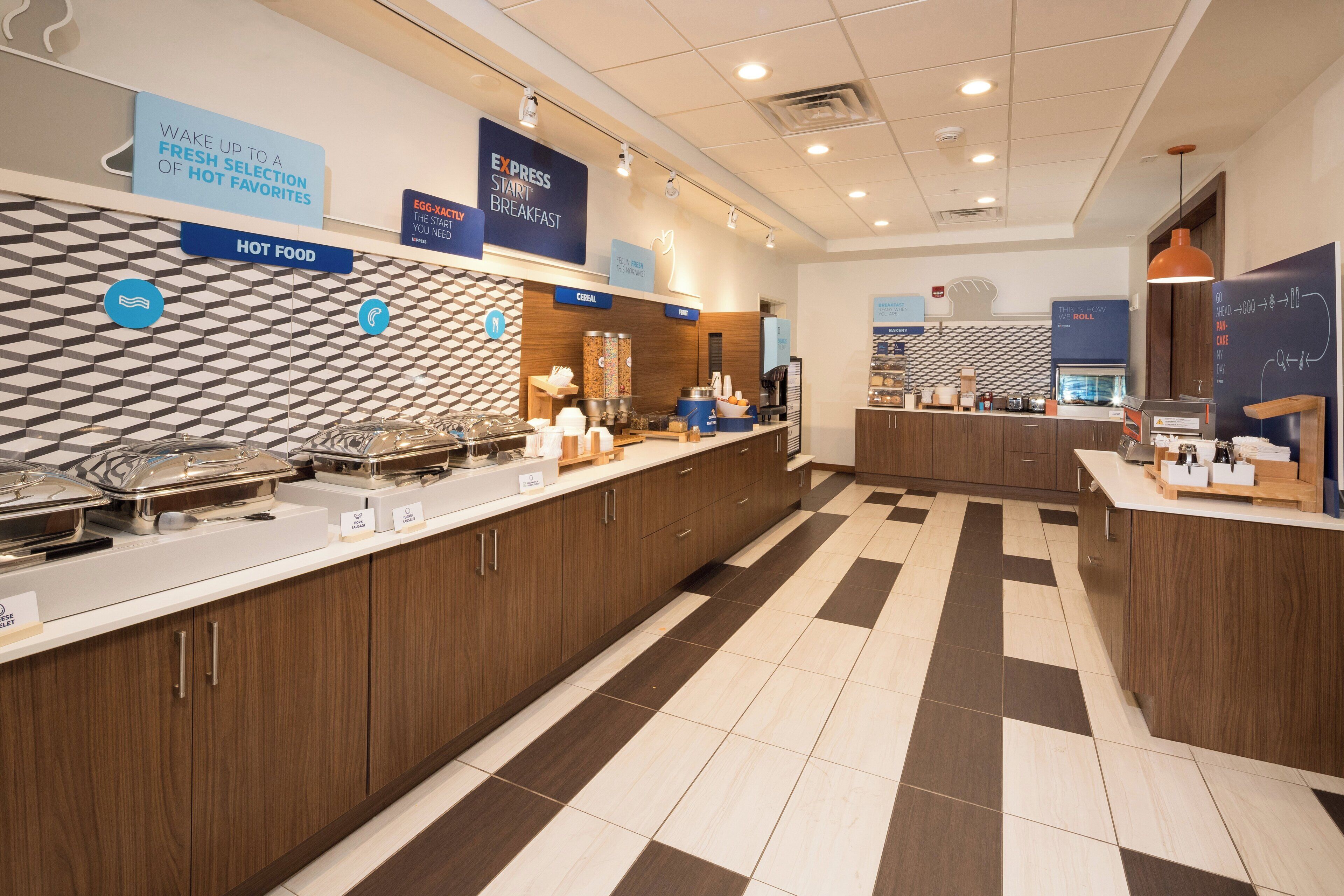 A hotel breakfast area with a buffet setup, including hot food and cereal options.