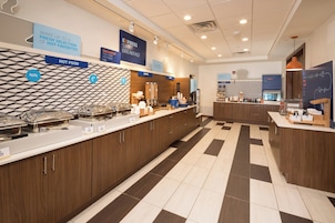 A hotel breakfast area with a buffet setup, including hot food and cereal options.