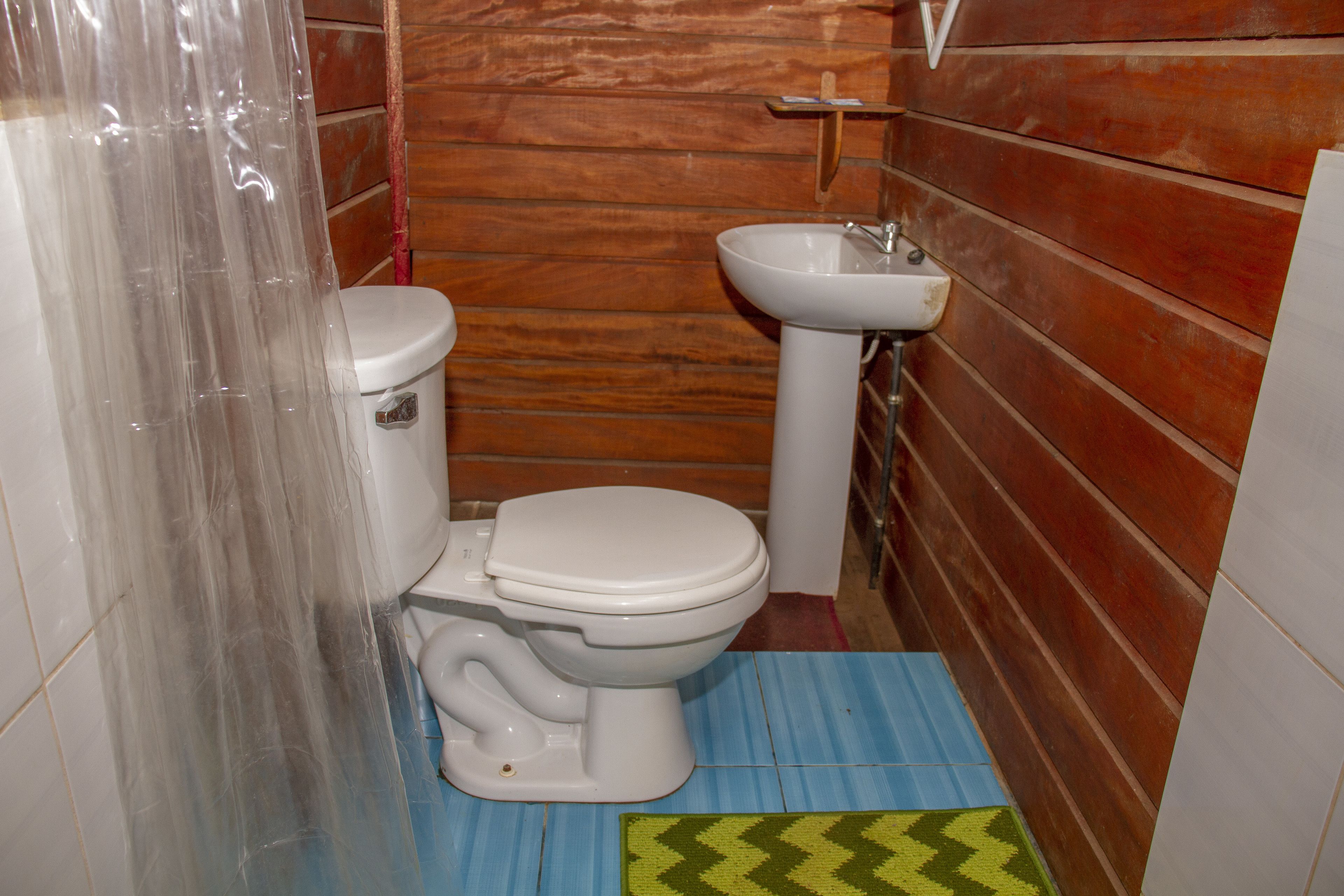 A small bathroom with a toilet, sink, and wooden walls.
