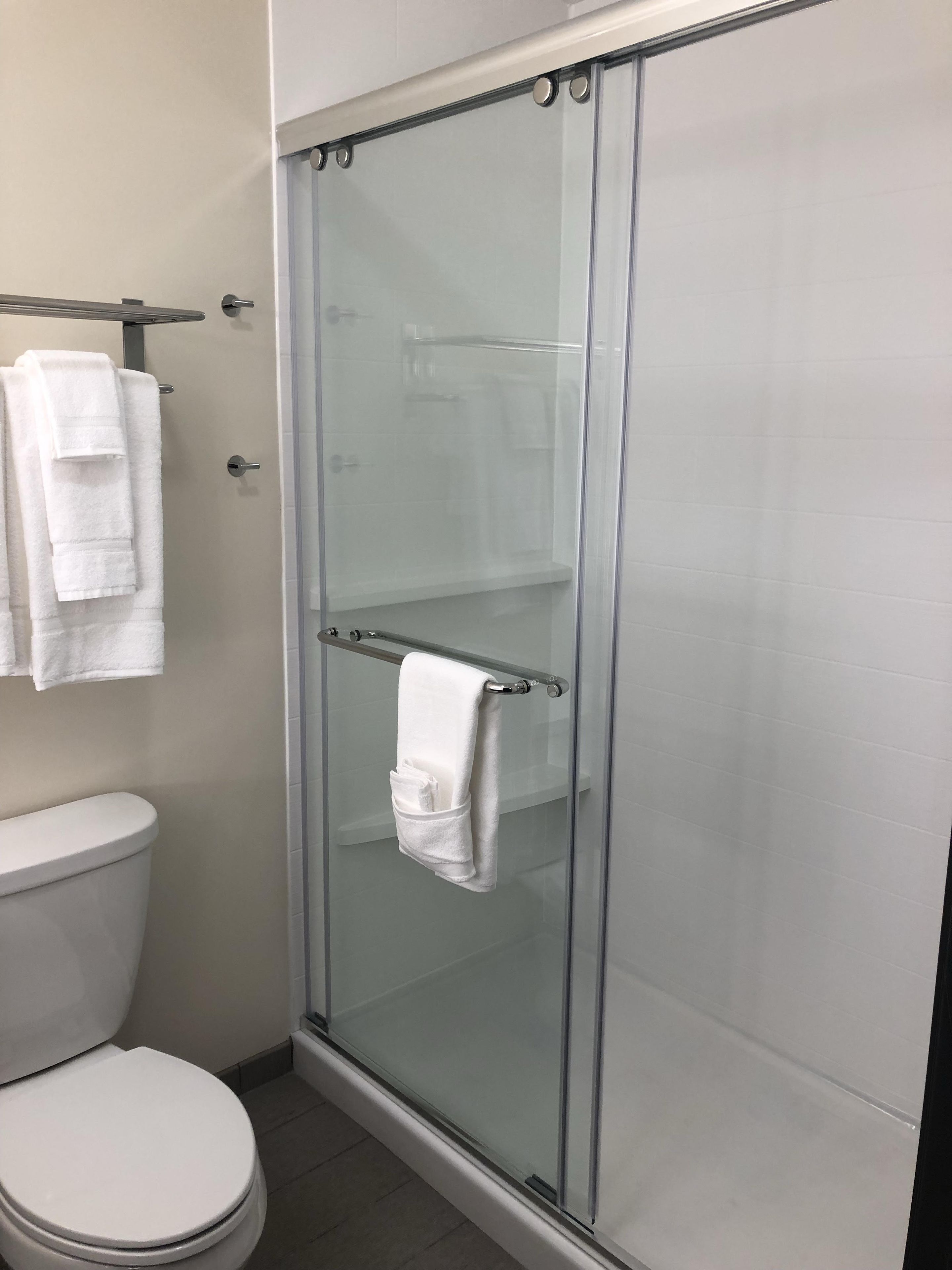 A modern bathroom with a glass-enclosed shower, a toilet, and a towel rack with multiple towels.
