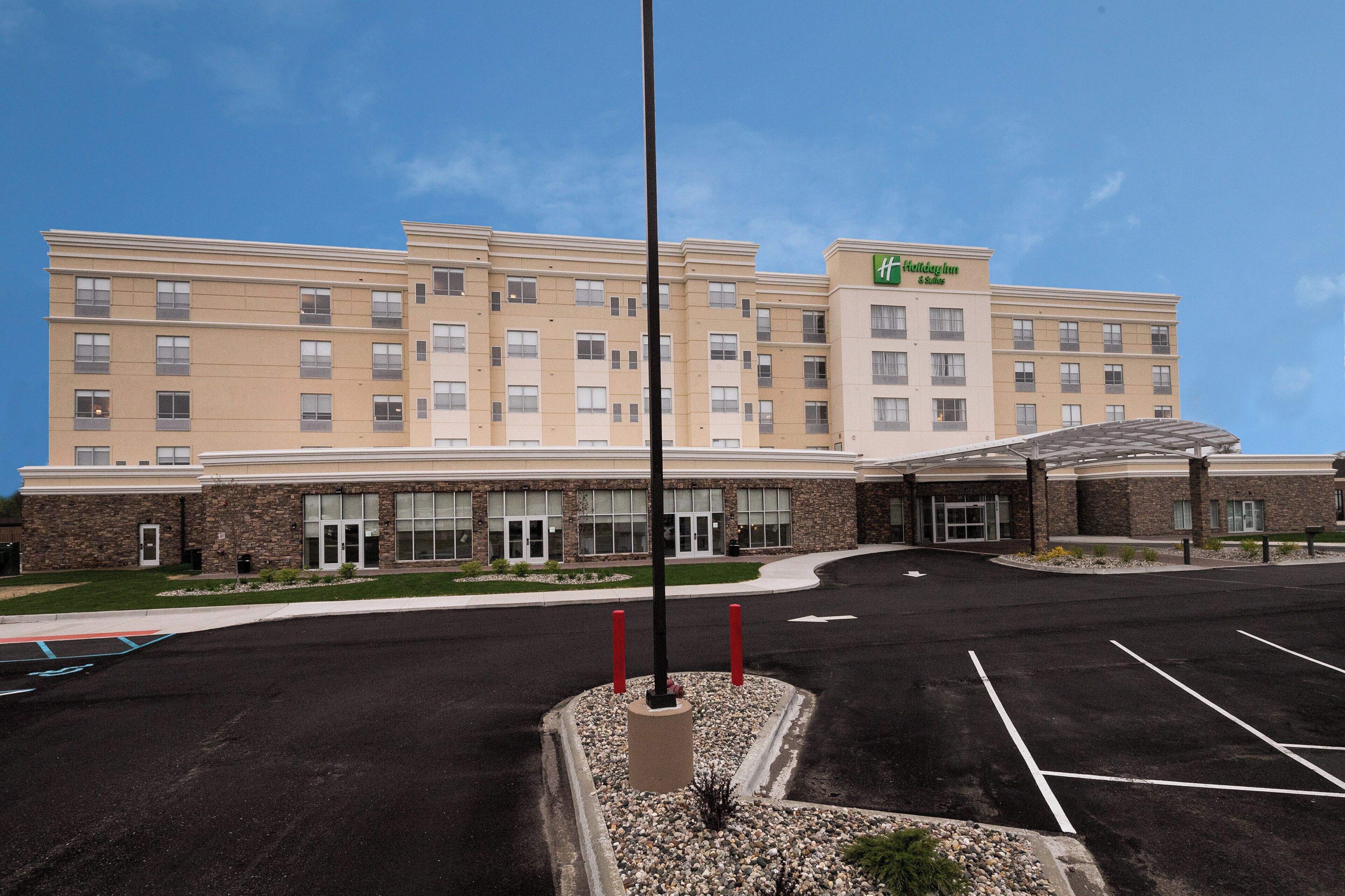 A multi-story hotel with a central entrance, a covered parking area, and a clear sky.