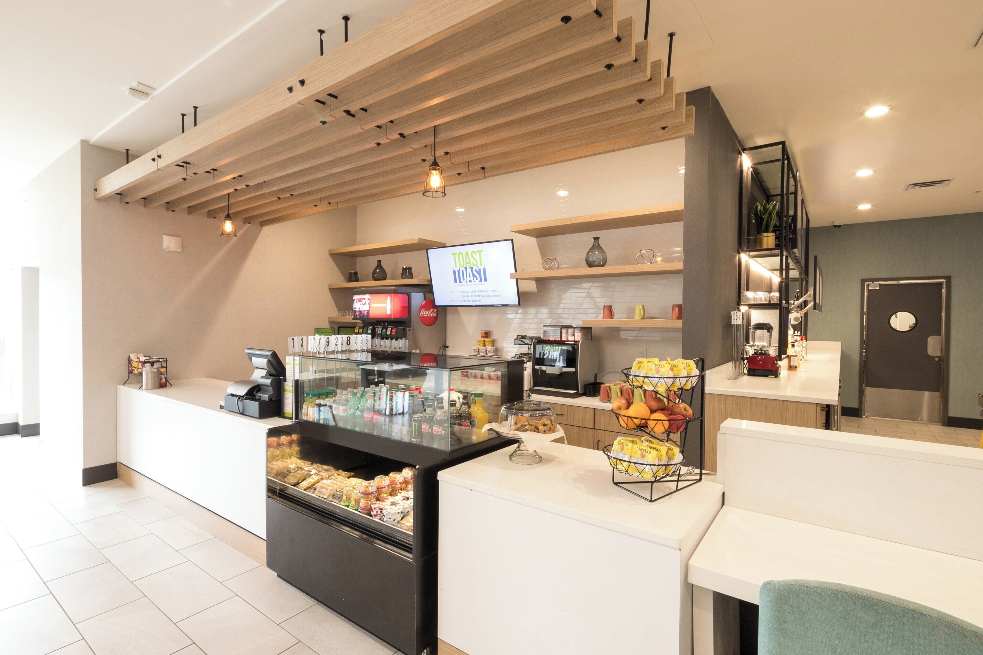 Una barra de desayuno con una pantalla digital de menú, un dispensador de bebidas y una exhibición de frutas.
