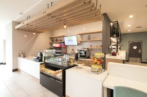 Una barra de desayuno con una pantalla digital de menú, un dispensador de bebidas y una exhibición de frutas.