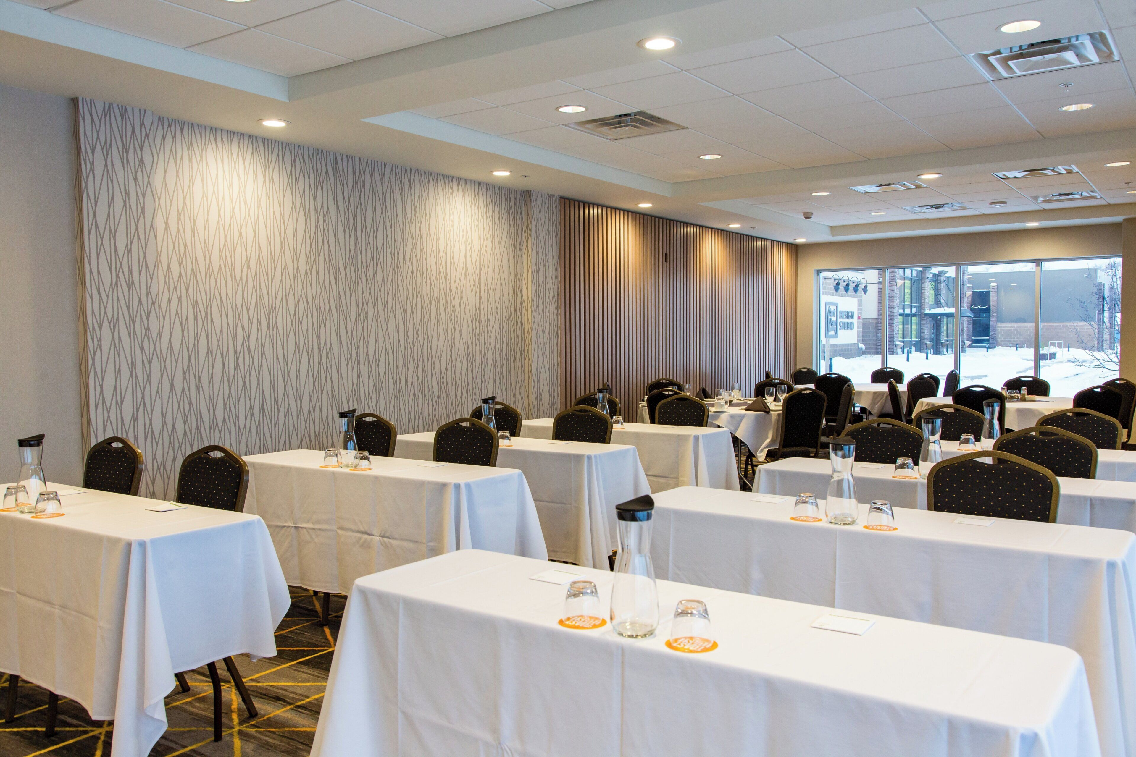 A conference room with multiple tables and chairs, large windows, and a patterned wall.