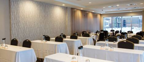 A conference room with multiple tables and chairs, large windows, and a patterned wall.