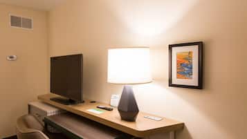 Ein Hotelzimmer mit Schreibtisch, Fernseher, Lampe, einem gerahmten Bild und einem Thermostat an der Wand.