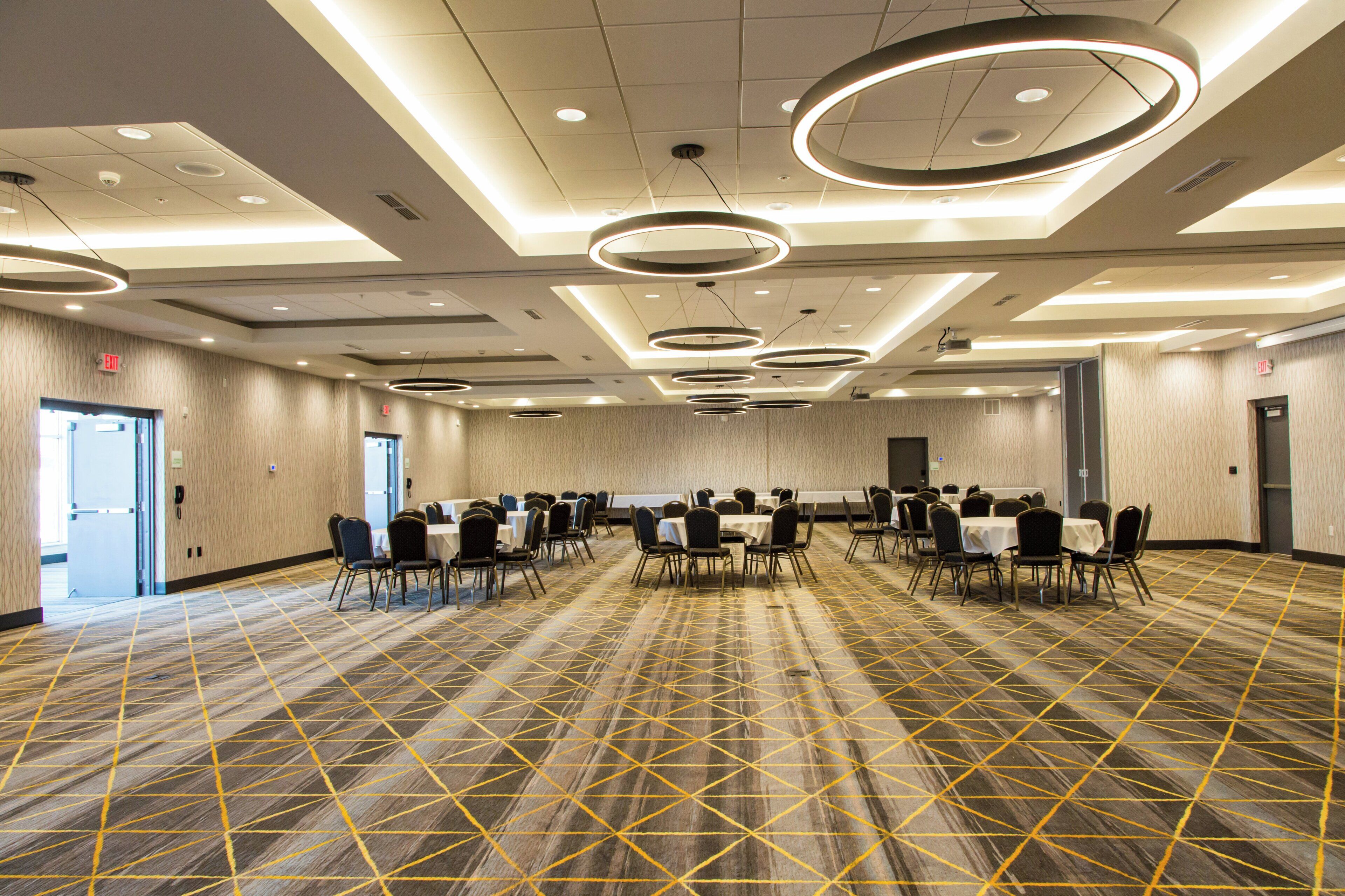 A conference room with multiple tables and chairs, a patterned carpet, and modern circular ceiling lights.