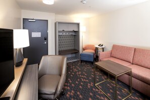A hotel room with a sofa, a chair, a small table, a TV, a lamp, a door, and a kitchenette area. - Holiday Inn Hotels and Suites Mount Pleasant by IHG (Mount Pleasant)