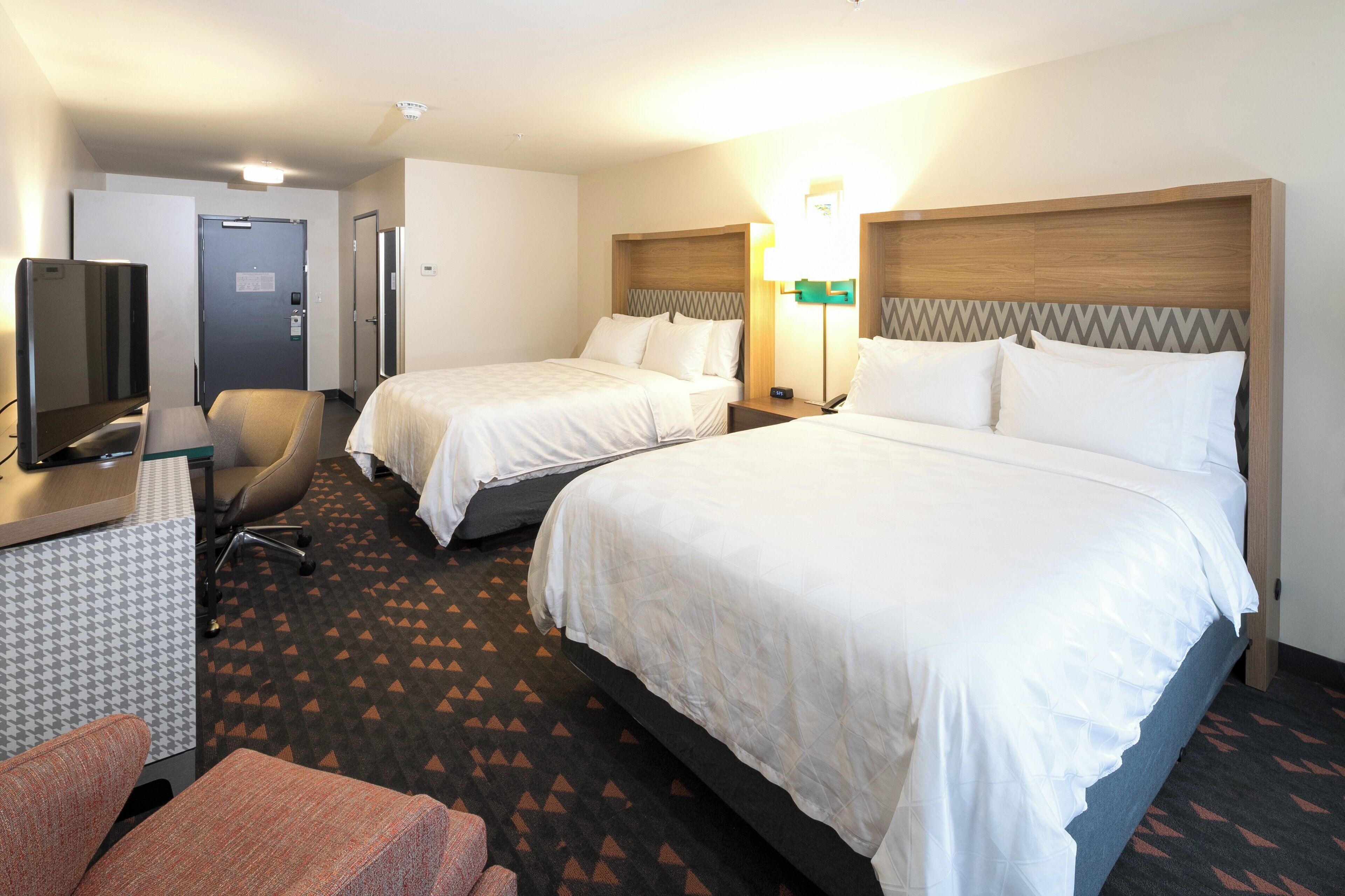 A hotel room with two beds, a desk with a television, and a chair.