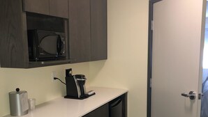 Una cocina compacta con armarios de madera oscura, un microondas, una cafetera y una puerta blanca.