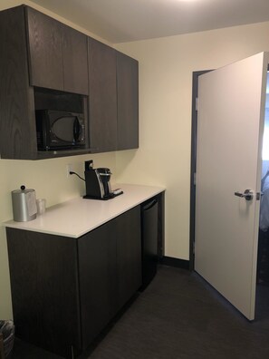 A compact kitchen with dark wood cabinets, a microwave, a coffee maker, and a white door. - Holiday Inn Hotels and Suites Mount Pleasant by IHG (Mount Pleasant)