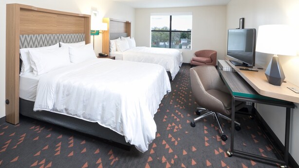 Habitación de hotel con dos camas, un escritorio con televisor y vistas al exterior.