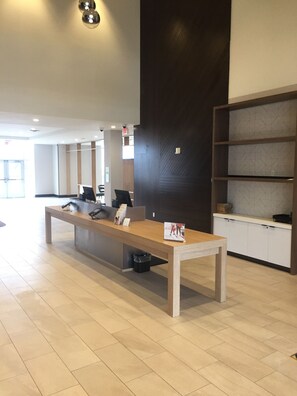 A reception desk with a computer, brochures, and a trash bin. There is a dark wall with a geometric pattern and a white cabinet with drawers. - Holiday Inn Hotels and Suites Mount Pleasant by IHG (Mount Pleasant)